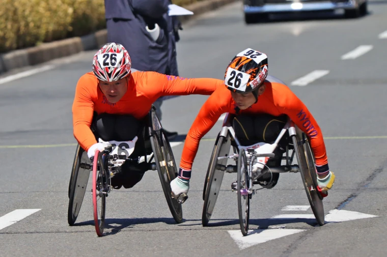 車いす駅伝大会中、選手二人がコース上を車いすで走っている。