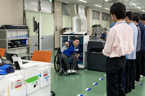 工場内で車椅子の作業者から説明を受けている。